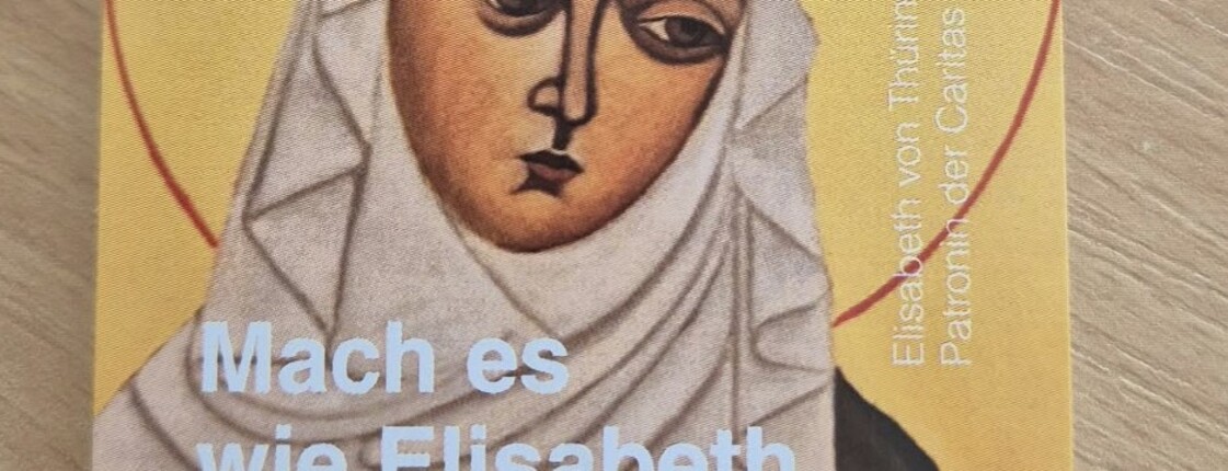Eine Einkaufsmünze aus Holz mit dem Schriftzug "Caritas&Du" liegt auf einer Verpackung mit dem Abbild der heiligen Elisabeth.