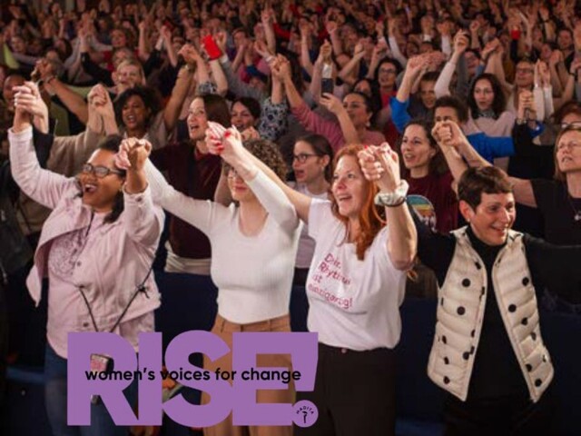 Eine große Menschenmenge hebt gemeinsam die Hände, während im Vordergrund mehrere Personen eng beieinanderstehen und das violette „RISE! women’s voices for change“-Logo eingeblendet ist.
