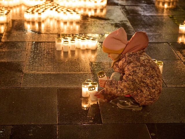 Kind in Winterkleidung stellt Kerzen auf nassem Platz auf; tausende Lichter als Zeichen der Solidarität mit der Ukraine in Österreich.