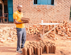 Arbeiter hält CO₂-neutrale Ziegel vor Schulgebäude im Südsudan