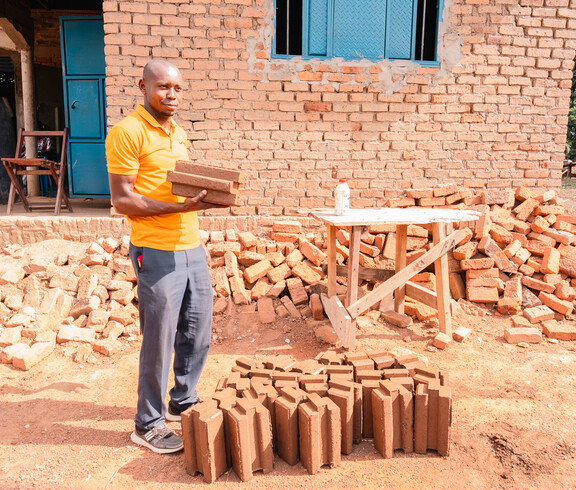 Arbeiter hält CO₂-neutrale Ziegel vor Schulgebäude im Südsudan