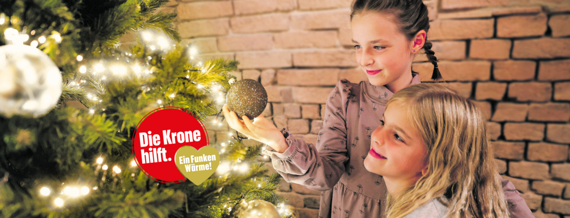 Zwei Mädchen beim Christbaum - und ein Logo "Die Krone hilft. Ein Funken Wärme"