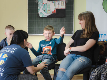 Kleine Kinder und Betreuerinnen sitzen gemeinsam in einem Klassenraum im Sesselkreis.