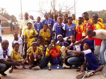 Gruppe von Sportlerinnen und Sportlern mit Behinderungen in Sportkleidung zeigt stolz Medaillen und Pokale nach einem Turnier in der Demokratischen Republik Kongo.
