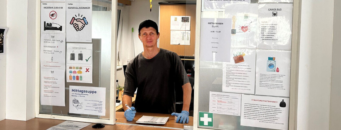 Mitarbeiter steht mit Stift und Liste hinter Empfangsfenster.