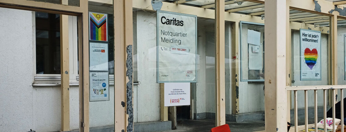 Eingangsbereich des Caritas Notquartiers Meidling mit Informationsschildern und Plakaten an der Fassade