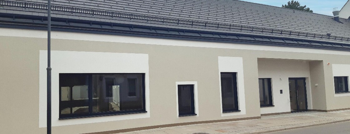 Vorderansicht des Caritas Wohnhauses Laa. Graue Fassade mit weißen Rahmen um die anthrazitgrauen Fenster. Ebenerdiges Gebäude