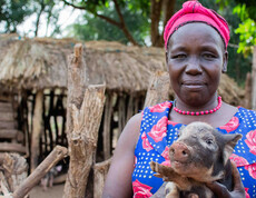 Landwirt*in hält Ferkel vor traditionellem Stall für Landwirtschaftsprojekt im Südsudan
