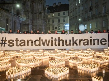 Kind in Winterkleidung stellt Kerzen auf nassem Platz auf; tausende Lichter als Zeichen der Solidarität mit der Ukraine in Österreich.