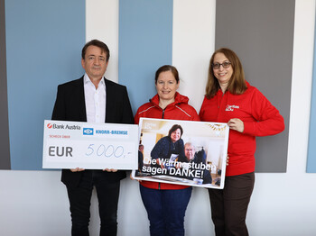 Drei Personen stehen vor einer Wand und präsentieren einen symbolischen Scheck über 5.000 Euro sowie ein Plakat mit der Aufschrift „Die Wärmestuben sagen DANKE!“.