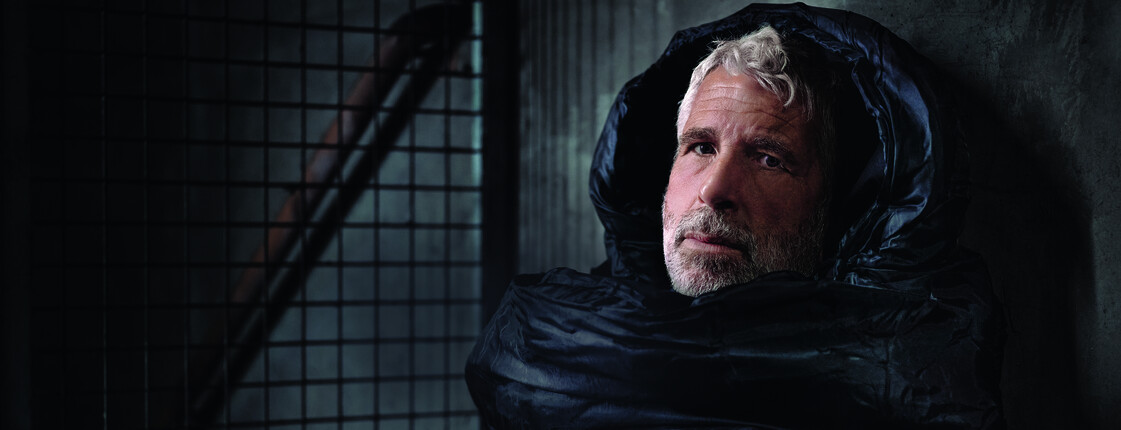 Der Fernsehmoderator Dirk Stermann als Obdachloser im Schlafsack abgebildet