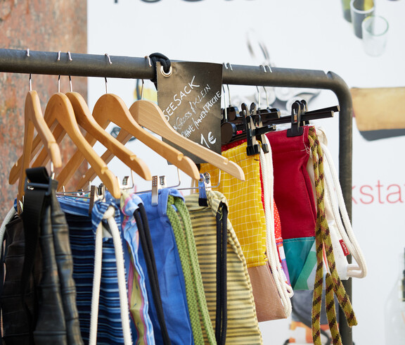 Bunte Upcycling-Turnbeutel an Kleiderstange beim Projekt reStart der Caritas, Preisschild mit 1 €