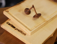 Schneidebrett mit Branding „Caritas preWork“ und zwei gedrechselte Holzkreisel als Beispiel für handwerkliche Arbeiten