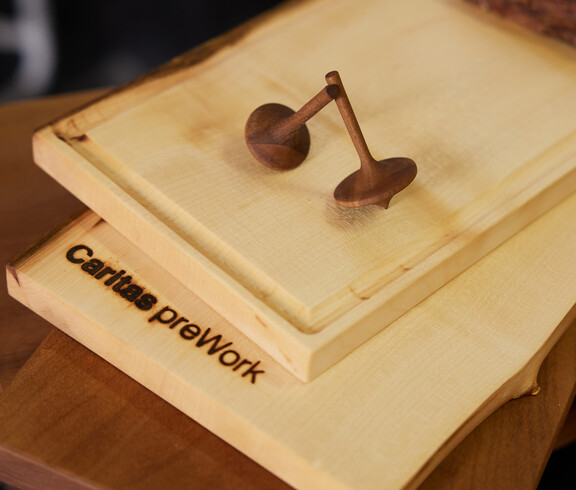 Schneidebrett mit Branding „Caritas preWork“ und zwei gedrechselte Holzkreisel als Beispiel für handwerkliche Arbeiten