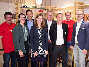 Gruppenfoto bei der Neueröffnung von „kunst.hand.werk“ in Wiener Neustadt: Acht Personen stehen in den Verkaufsräumen des Shops vor Holzregalen mit handgefertigten Produkten.