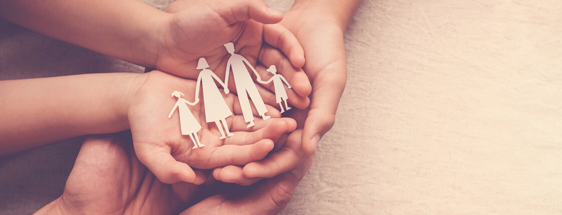 Mehrere Hände halten gemeinsam eine Papierfigur einer Familie, die Schutz und Zusammenhalt symbolisiert.