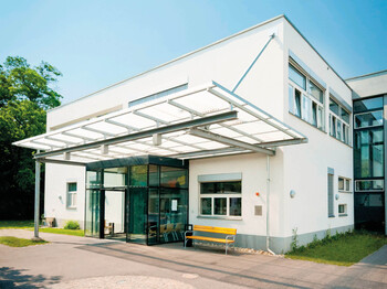 Außenansicht der Tagesstätte in Rannersdorf. Weißes Flachdachgebäude mit gläsernem Vordach