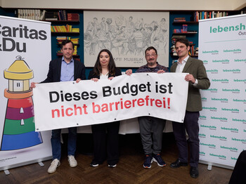 Vier Personen stehen mit einem Banner auf einem Podium.