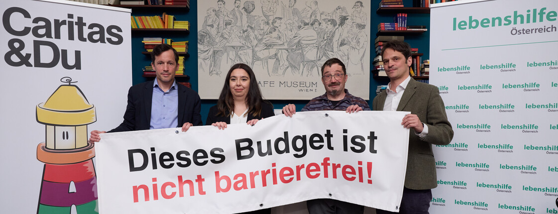 Vier Personen stehen mit einem Banner auf einem Podium.