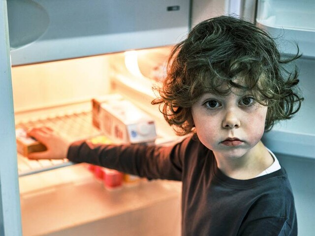 Ein Bub steht vor einem Kühlschrank, der fast leer ist
