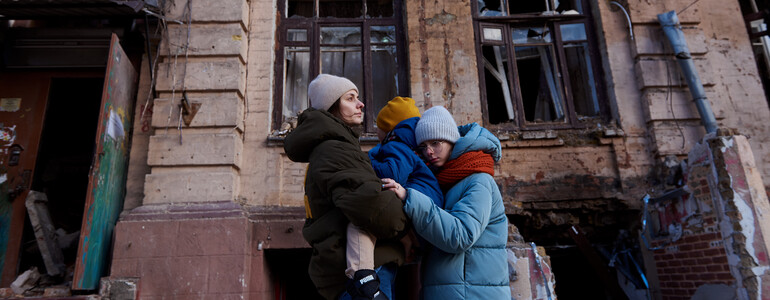 Frau mit Kindern steht vor zerstörtem Haus in Kiew Ukraine