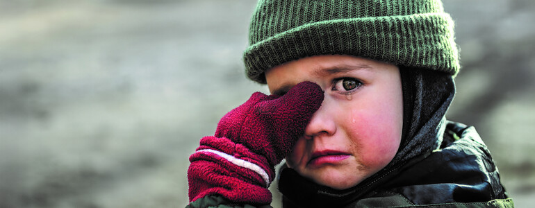 Kind mit Mütze und roten Handschuhen wischt sich weinend die Augen ab