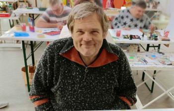 Künstler sitzt bei einem farbigen Bild im Atelier der Caritas-Kunstgruppe im Weinviertel.