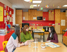 Drei Frauen sitzen im Lerncafé Wien an einem Tisch mit Plakat, Wassergläsern und Keksen, im Hintergrund eine Lernküche.