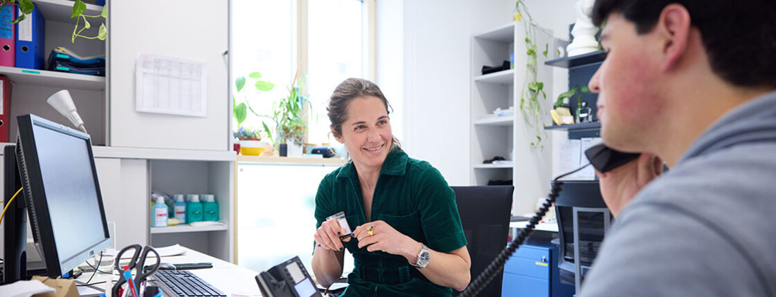 Mitarbeiterin spricht im JUCA-Büro mit jungem Erwachsenen, der telefoniert; Gesprächssituation mit Computer am Schreibtisch.