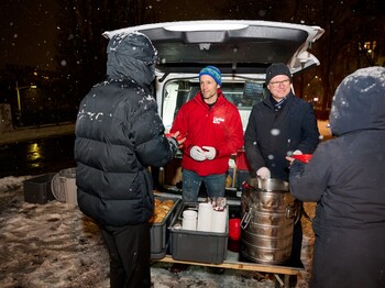 Zwei Caritas-Mitarbeiter geben beim Canisibus warme Suppe an obdachlose Menschen im Schneefall aus. © Drei-WirlPhoto