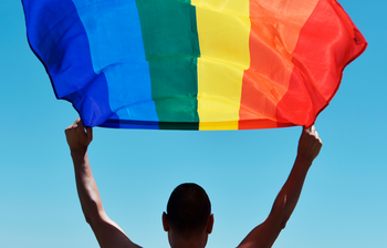 Person hält eine Regenbogenflagge als Symbol für queere Vielfalt, Sichtbarkeit und gesellschaftliche Teilhabe