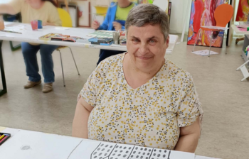 Künstlerin sitzt bei einem farbigen Bild im Atelier der Caritas-Kunstgruppe im Weinviertel.