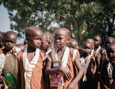 Gruppe von Grundschüler*innen in Uniform steht mit Heften auf Schulhof im Südsudan