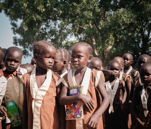 Gruppe von Grundschüler*innen in Uniform steht mit Heften auf Schulhof im Südsudan