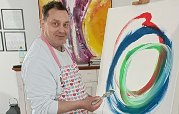 Künstler mit Pinsel malt ein farbiges Bild auf einer Leinwand im Atelier der Caritas-Kunstgruppe im Weinviertel.