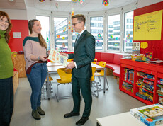 Drei Mitarbeiterinnen überreichen einem Mann im Anzug ein buntes Dankesplakat im Lerncafé der Caritas Wien.