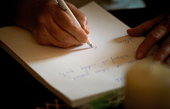 Eine Hand mit Kugelschreiber in der Hand schreibt etwas auf dein Blatt Papier.