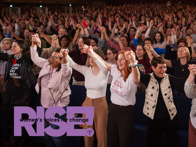 Eine große Menschenmenge hebt gemeinsam die Hände, während im Vordergrund mehrere Personen eng beieinanderstehen und das violette „RISE! women’s voices for change“-Logo eingeblendet ist.