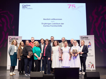 Gruppenfoto auf einer Bühne beim Festakt zum 75-jährigen Jubiläum der Caritas Familienhilfe. Mehrere Mitarbeitende und Gäste stehen vor einer Leinwand mit der Aufschrift „Herzlich willkommen zum 75-jährigen Jubiläum der Caritas Familienhilfe“