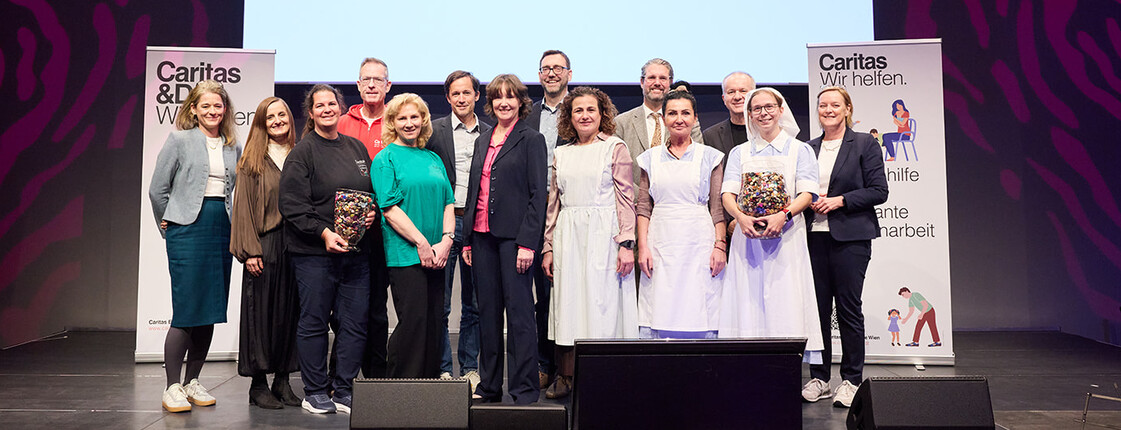 Gruppenfoto auf einer Bühne beim Festakt zum 75-jährigen Jubiläum der Caritas Familienhilfe. Mehrere Mitarbeitende und Gäste stehen vor einer Leinwand mit der Aufschrift „Herzlich willkommen zum 75-jährigen Jubiläum der Caritas Familienhilfe“