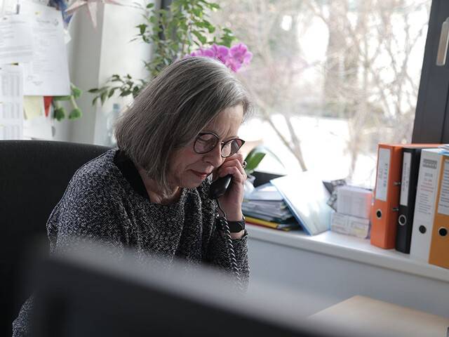 Person sitzt in einem Büro am Telefon und notiert Informationen. Die Aufnahme steht für Erreichbarkeit, Beratung, Unterstützung und Hilfe in sozialen Notlagen.