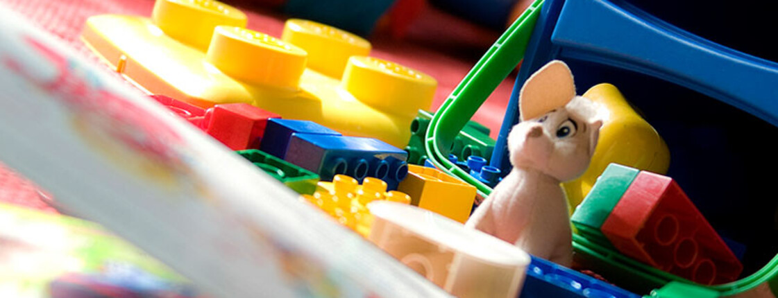 Spielzeug, Bauklötze und Kinderbücher liegen auf einer Spieldecke. Die Aufnahme zeigt den Spielbereich eines Familienzentrums für Kinder und Familien.