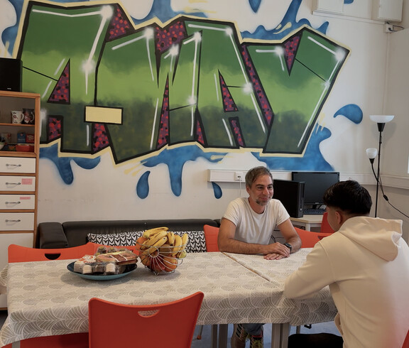 Zwei Männer unterhalten sich an einem Tisch in einem bunt gestalteten Gemeinschaftsraum der Einrichtung a_way