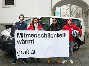 Ein Ex-Klient, Judith Hartweger, Christopher Seiler und Klaus Schwertner halten Schlafsäcke und ein Transparent mit der Aufschrift Mitmenschlichkeit wärmt