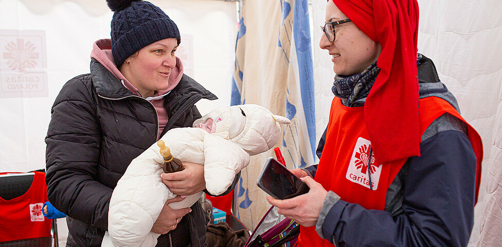 Eine Frau hält ein Baby im Arm, sie spricht mit einem Caritas-Mitarbeiter